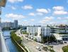 Elevated balcony featuring a metal railing, overlooking urban skyline, water channel, and infrastructure