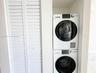 Stacked white laundry appliance set enclosed within a built-in alcove featuring white louvered bifold doors