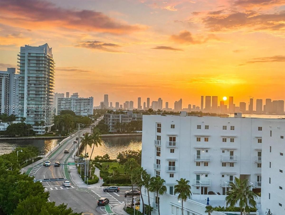 Aerial perspective featuring a multi-story white stucco exterior with recessed balconies and a skyline backdrop