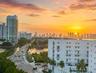 Aerial perspective featuring a multi-story white stucco exterior with recessed balconies and a skyline backdrop