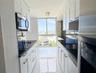 Galley kitchen featuring white Shaker-style cabinetry, dark stone countertops, stainless steel appliances, large-format tile flooring, and floor-to-ce