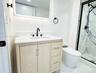 Light wood-finish vanity with a white countertop, undermount sink, matte black faucet, and walk-in shower featuring patterned tile surrounds and a mat