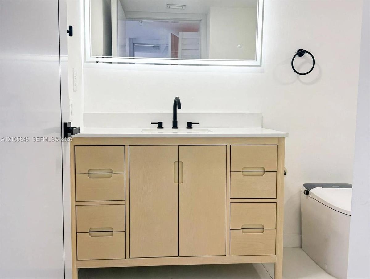 Light-toned wood vanity with integrated storage drawers and cabinets, topped with a solid-surface countertop and undermount sink