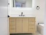 Light-toned wood vanity with integrated storage drawers and cabinets, topped with a solid-surface countertop and undermount sink