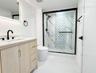 Light wood-finish vanity with a white countertop, walk-in shower with patterned tile inlay, glass enclosure with matte black hardware, and matching ma