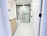 Bathroom featuring a light wood-finish vanity, large-format tile flooring, and a glass-enclosed shower with decorative accent tile, stone-patterned wa
