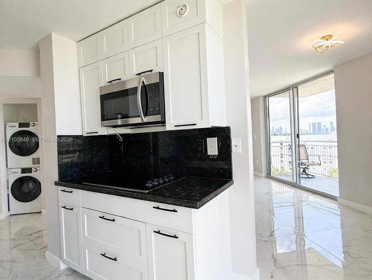 Kitchen featuring white shaker cabinetry, dark stone countertops, integrated stainless steel microwave, and polished tile flooring