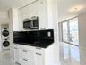 Kitchen featuring white shaker cabinetry, dark stone countertops, integrated stainless steel microwave, and polished tile flooring