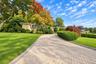 Brick exterior featuring a paved stone driveway, manicured landscaping, mature trees, and bay windows
