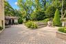 Expansive stone-paver patio featuring a built-in spa, tiered retaining walls, and mature landscaping