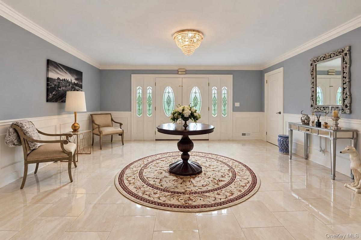 Foyer featuring large-format tile flooring, double doors with decorative glass inserts, crown molding, and wainscoting, accented by a tiered crystal-s
