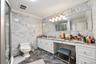 Full-bathroom featuring natural stone wall and floor tiling, expansive vanity with integrated stone countertop, crown molding, and multi-bulb wall-mou