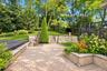 Paver patio featuring stone retaining walls, integrated stairs, tiered landscaping, and mature trees