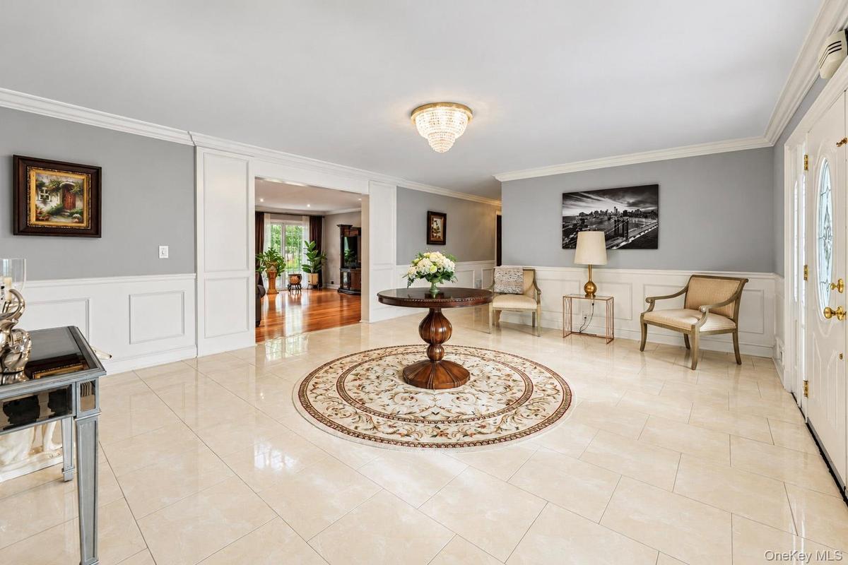 Foyer featuring large-format tile flooring, crisp wainscoting, crown molding, a decorative crystal-style ceiling fixture, and a white entry door with 