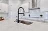 Quartz counters, undermount sink, matte black faucet, and herringbone tile backsplash with a view into the home.