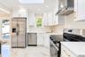 Kitchen featuring white shaker-style cabinetry, gold-tone hardware, stainless steel appliances, white stone-finish countertops with matching backsplas