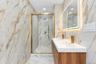 Dual vanity with integrated sinks, wall-to-wall large-format porcelain tile, walk-in shower with sliding glass door, brass-finish fixtures, and integr