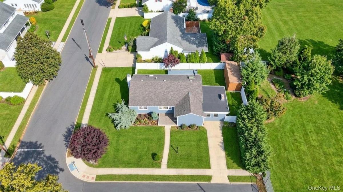 Aerial perspective featuring a corner lot, concrete driveway, stone walkway, exterior storage shed, and white privacy fencing