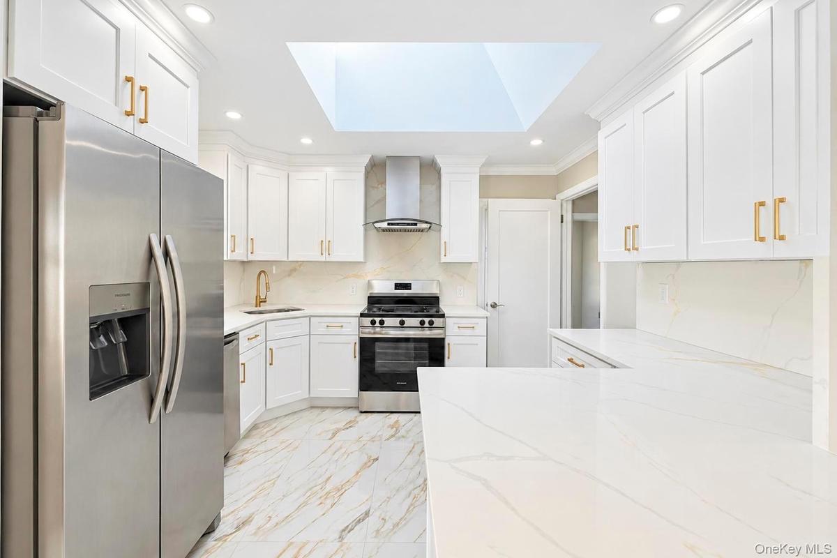 Kitchen featuring white shaker-style cabinetry, stainless steel appliances, quartz countertops, a large skylight, and stone-finish tile flooring