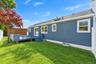 Exterior featuring blue horizontal siding, raised wooden deck, manicured lawn, white vinyl fencing, and a detached storage structure