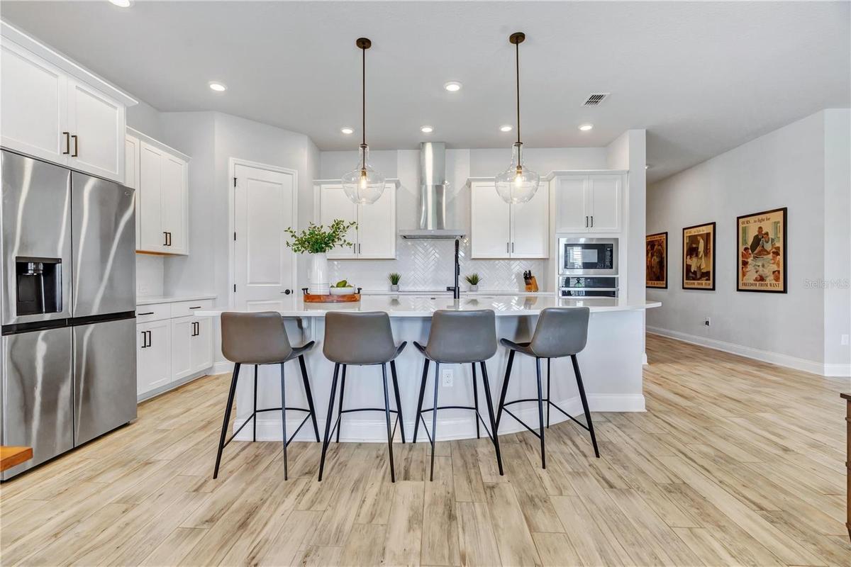 Chef inspired kitchen with an expansive Calacatta Arno quartz island, seating for four, statement pendants, stainless appliances, and a built in wall 