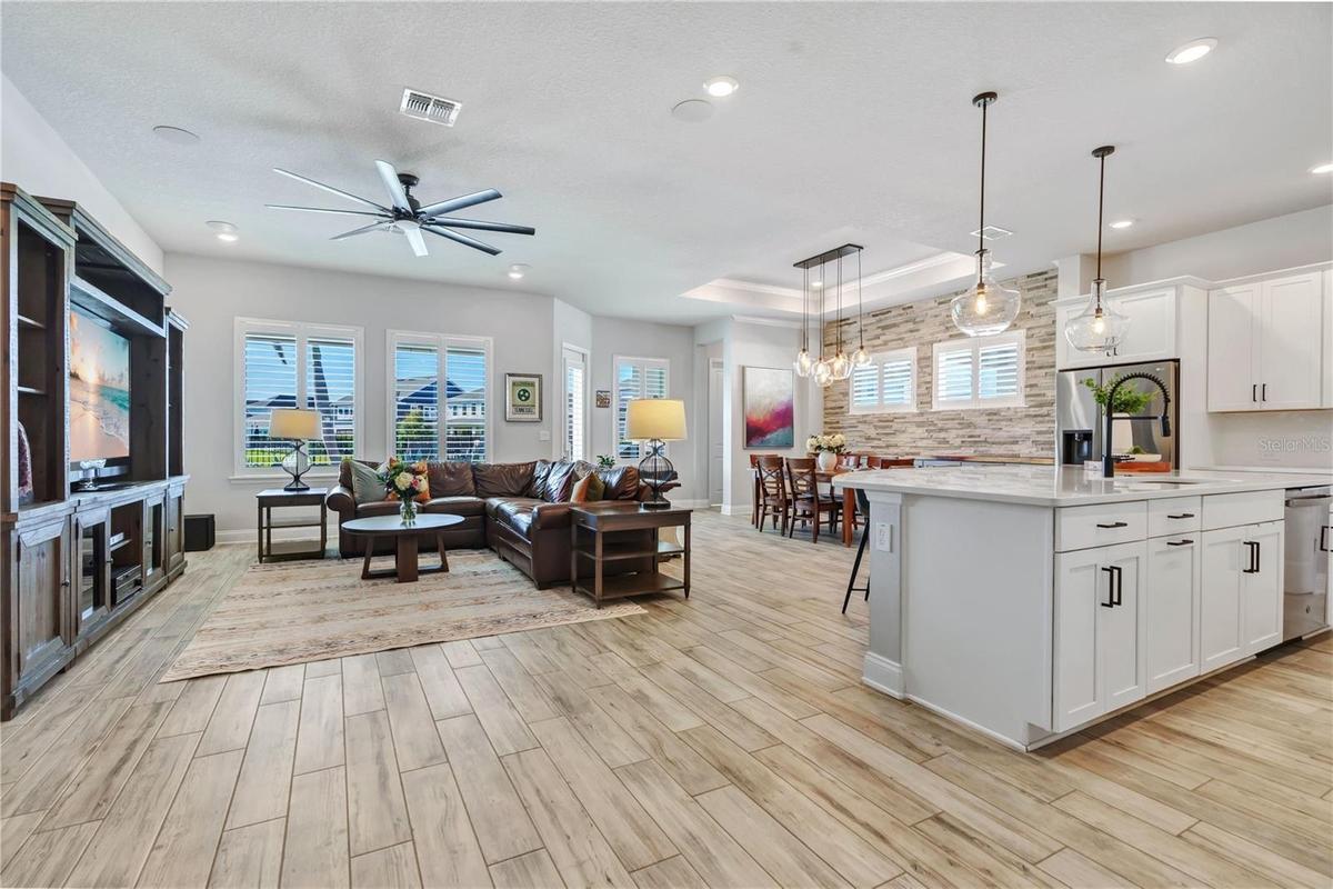 Open floor plan connecting the great room, kitchen, and dining area. Wood look plank tile, crown moulding, and natural light throughout this one story