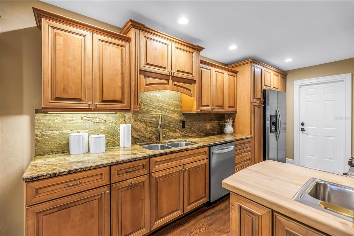 This custom kitchen features solid wood cabinetry, granite countertops, and a matching backsplash. It is equipped with updated stainless steel applian