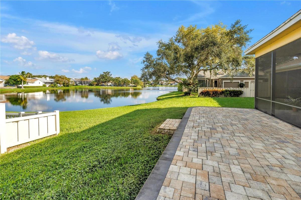 The elevated paver patio at the rear of the property overlooks a scenic grassy knoll and provides an expansive view of the lake, which serves as a nat