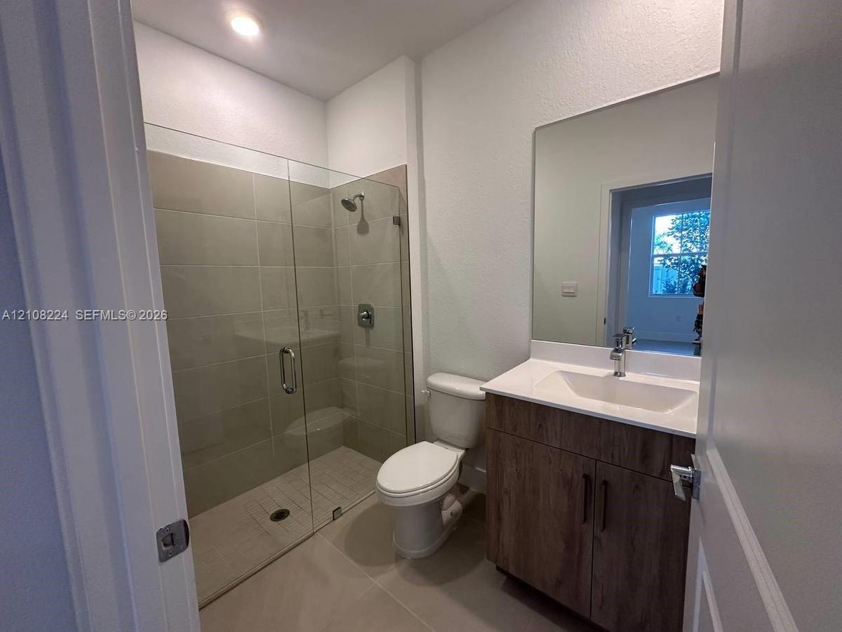 Kitchen featuring wood-finish cabinetry, quartz countertops, a stone-tile backsplash, stainless steel appliances, and large-format tile flooring