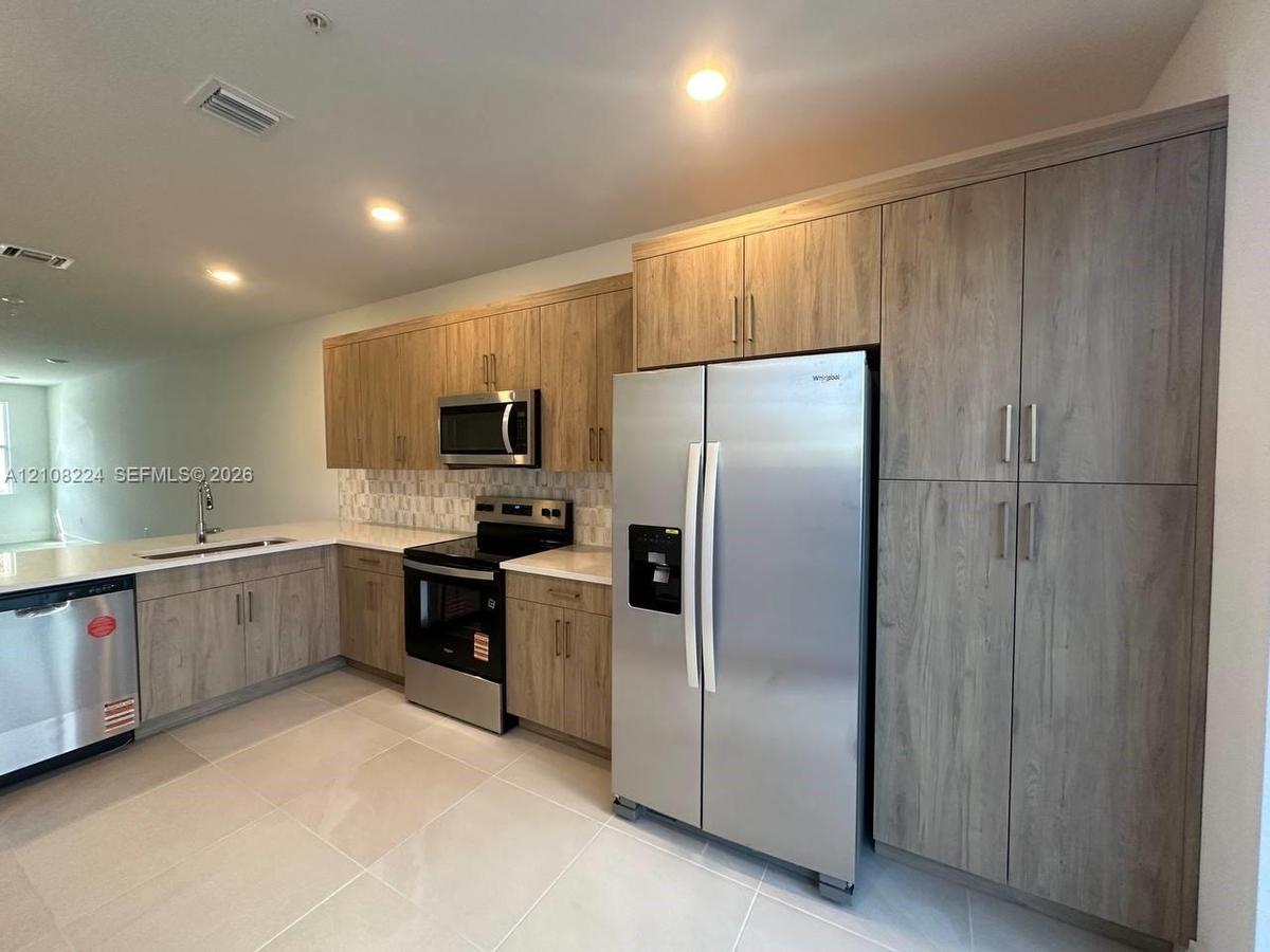 Kitchen featuring textured wood-finish cabinetry, stainless steel appliances, light-toned solid surface countertops, a decorative mosaic tile backspla