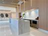Custom kitchen area featuring stone slab countertops, waterfall-edge island, integrated cabinetry, light-toned wood paneling, and vertical recessed li