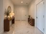 Large-format polished stone flooring with neutral veining, high ceilings with recessed lighting, and crisp white interior doors