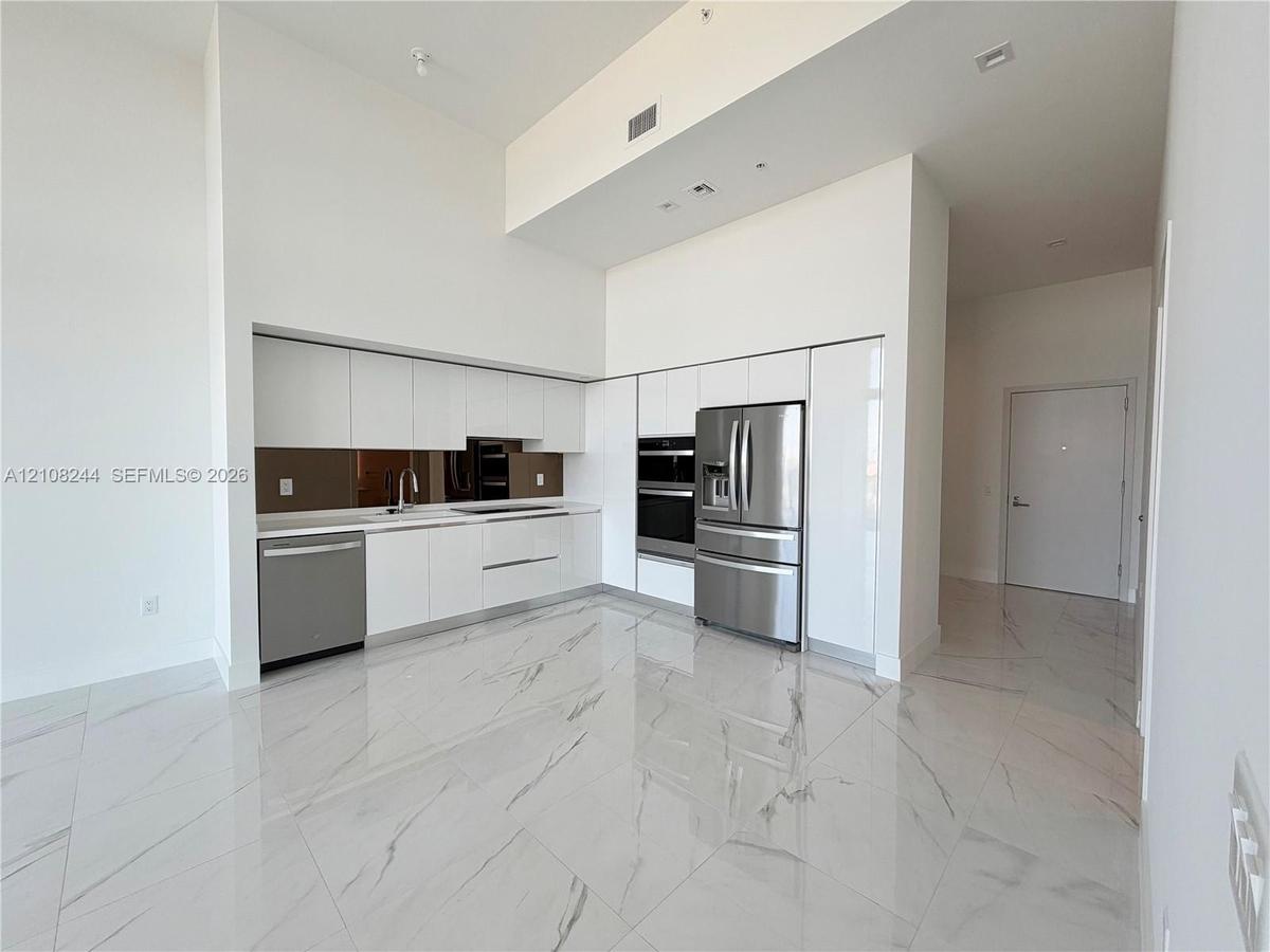 Kitchen featuring high-gloss white cabinetry, stainless steel appliances, built-in wall oven, metallic backsplash, and large-format porcelain tile flo