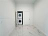 Dedicated utility space featuring stone-finish floor tile, a recessed laundry closet, and a stackable washer and dryer unit