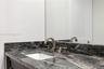 Stone countertop with integrated backsplash, under-mount basin, and metallic widespread faucet, complemented by a wall-mounted mirror