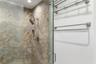 Walk-in shower featuring large-format tile surround, adjustable handheld shower fixture, built-in recessed storage niche, frameless glass door, and br