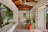 Covered patio featuring an exposed wood-beam ceiling, tile flooring, built-in bench seating, and an ornamental metal gate