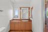 Bathroom featuring a stone-topped vanity with wood cabinetry, an integrated sink, dual wall-mounted light fixtures, and stone flooring