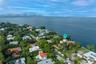 Aerial perspective of a waterfront property featuring direct water frontage, a multi-story residence with a red tile roof, and mature perimeter landsc