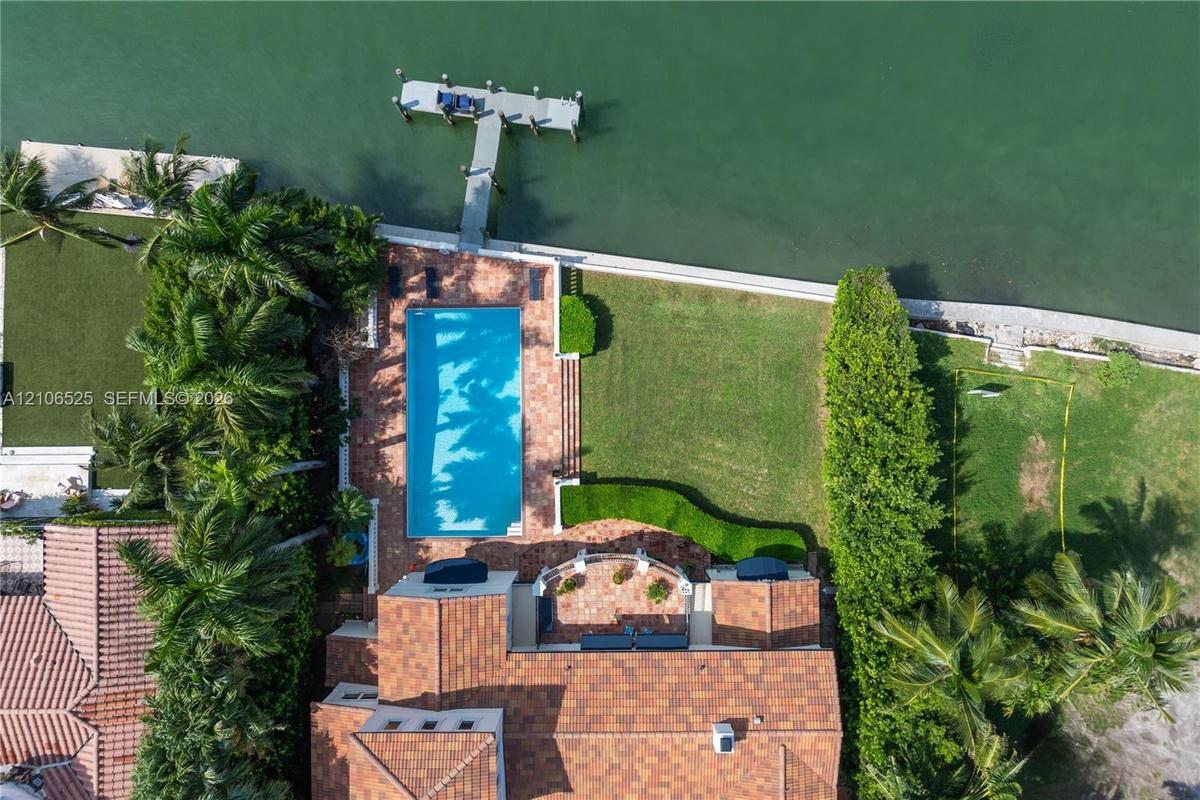 Waterfront property featuring a rectangular swimming pool, terracotta-tiled patio, private boat dock, and manicured lawn