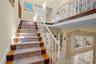 Staircase featuring wood-finish treads, decorative metal railings, and a second-level balcony overlooking a stone-accented arched entryway with tiled 