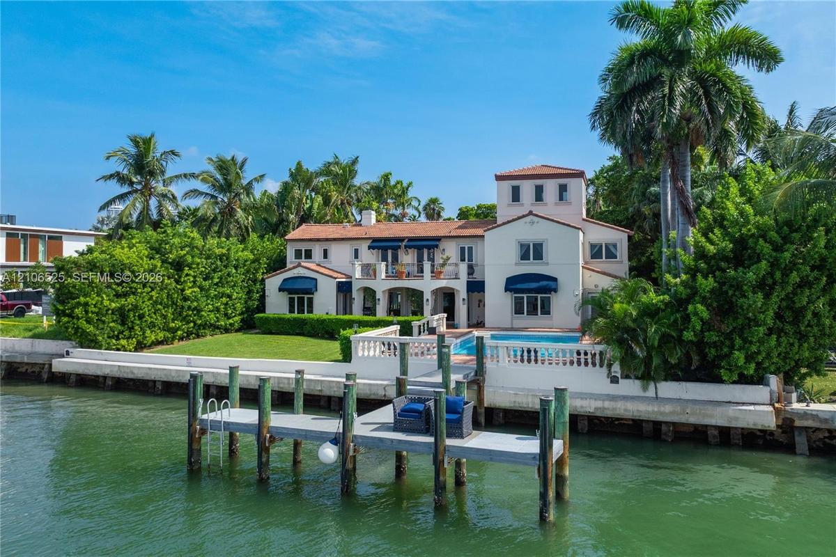 Waterfront residence featuring a private dock, swimming pool, second-story balcony, and terracotta-style roof tiles