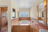 Bathroom featuring a built-in soaking tub, natural stone tile surround, walk-in shower with stone tile walls, stone-topped vanity, and wall-mounted li