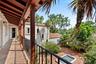 Covered balcony featuring exposed wood beam ceilings, wrought-iron railings, and tile flooring, overlooking a paved courtyard with a built-in stone fo