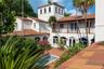 Mediterranean-style exterior featuring a stucco facade, clay tile roof, central courtyard, second-story balcony with metal railing, and a built-in sto