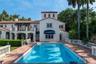 Stucco exterior residence featuring a tile roof, second-story balcony, expansive pool area, and classic balustrade hardscaping