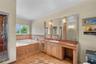 Bathroom featuring a stone-clad jetted soaking tub, custom wood cabinetry with a stone countertop, a recessed vanity area, integrated wall-to-wall mir