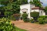 Stucco exterior featuring arched stone entryway detail, tile roof, and expansive terracotta-style paved patio area surrounded by mature landscaping