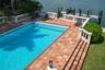 In-ground swimming pool featuring a terra-cotta tile deck, a balustrade perimeter railing, and a private wooden dock extending over the water