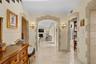 Foyer featuring arched stone-trimmed doorways, crown molding, stone tile flooring, and wall-mounted light fixtures